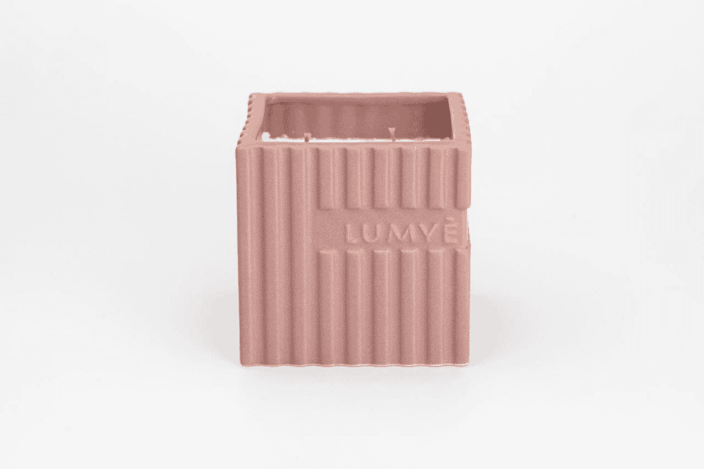 Kwadratowa różowa świeca w ceramicznym naczyniu.
